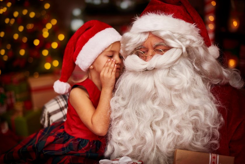 Kinder Weihnachtslieder: Mädchen mit Weihnachtsmütze flüstert Weihnachtsmann etwas ins Ohr