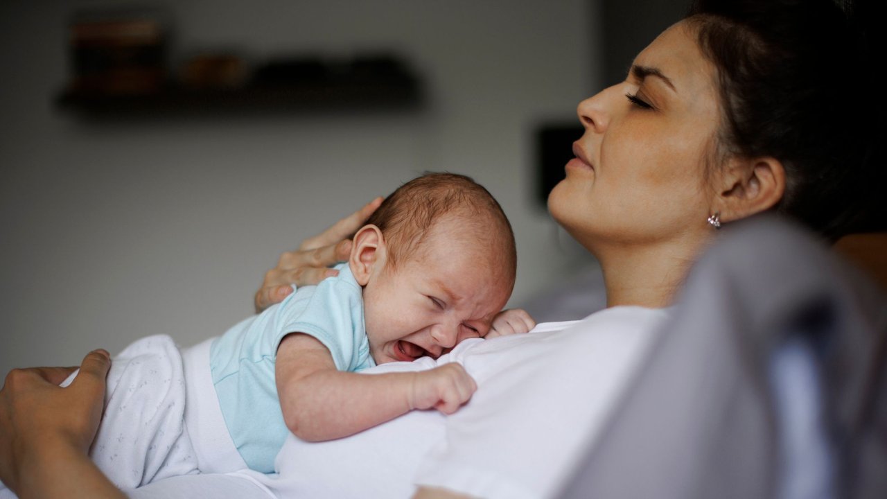 Test Wochenbettdepression: Mutter mit Neugeborenem schaut leidend