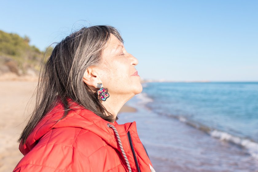 Anti-Stress-Tipps für Boomer: Frau atmet am Strand tief durch Anti-Stress-Tipps für Boomer: Frau atmet am Strand tief durch