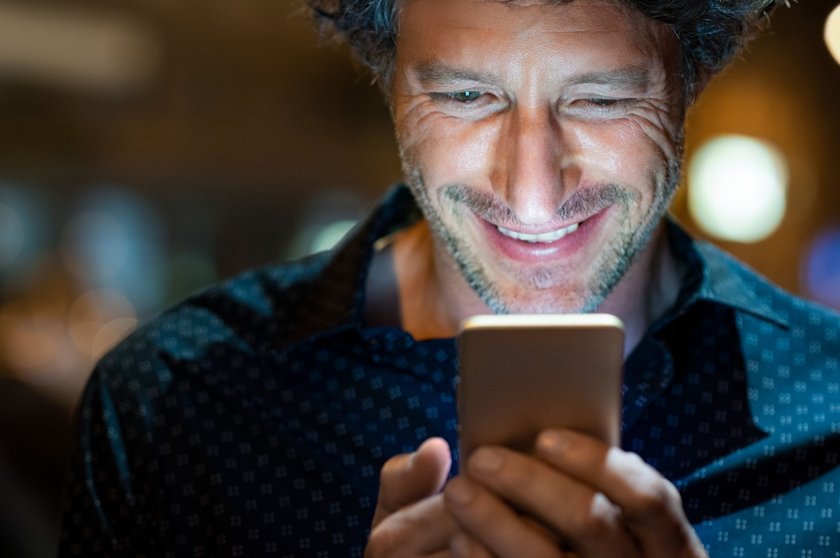Guten Abend Sprüche: Mann schaut lachend auf sein Handy am Abend