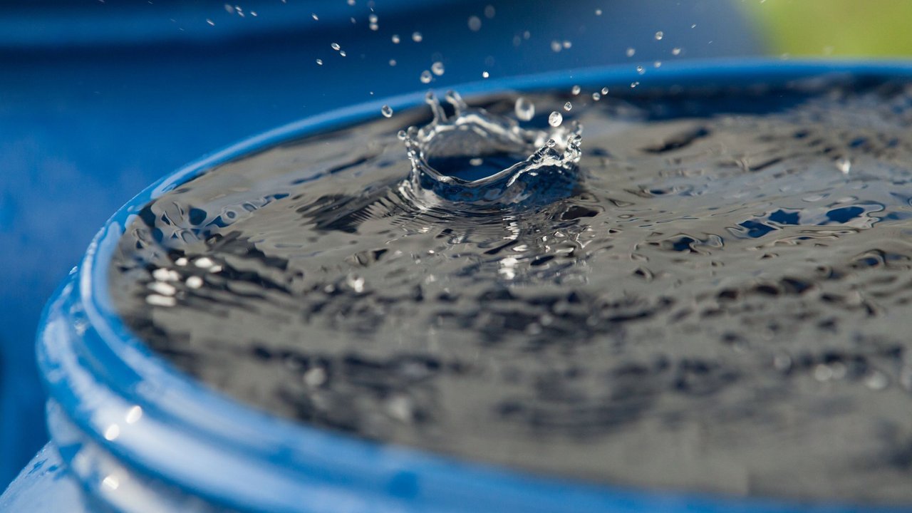Ein Regentropfen trifft auf die Wasseroberfläche einer vollen Regentonne Ein Regentropfen trifft auf die Wasseroberfläche einer vollen Regentonne