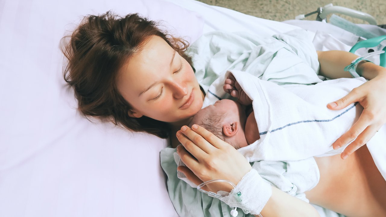 Frau kuschelt mit Neugeborenem im Zimmer der Geburtsklinik