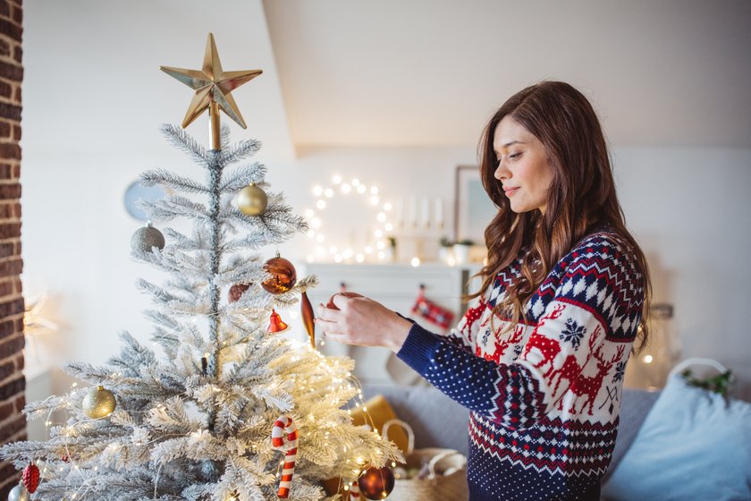 Young woman celebrating Christmas at home and decorating Christmas tree. Home is decorated with Christmas ornaments and lights. Young woman celebrating Christmas at home and decorating Christmas tree. Home is decorated with Christmas ornaments and lights.