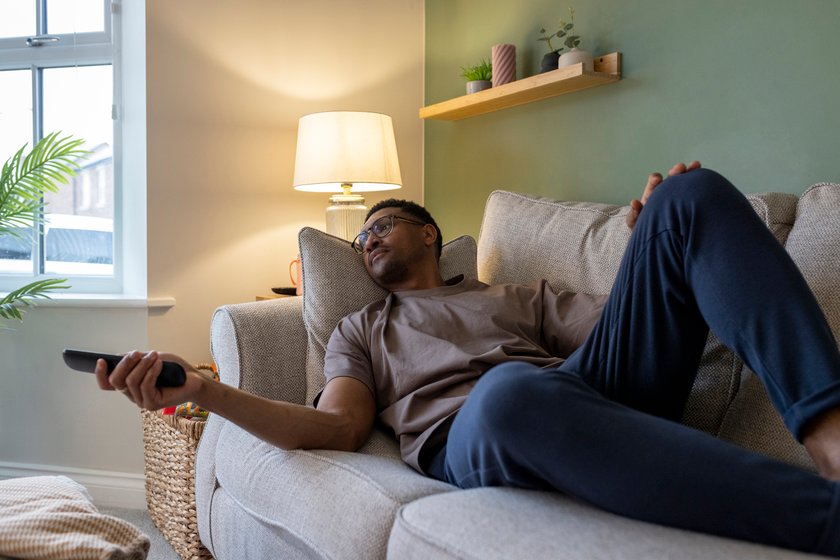 Mann liegt alleine auf dem Sofa und schaut fernsehen. Mann liegt alleine auf dem Sofa und schaut fernsehen.