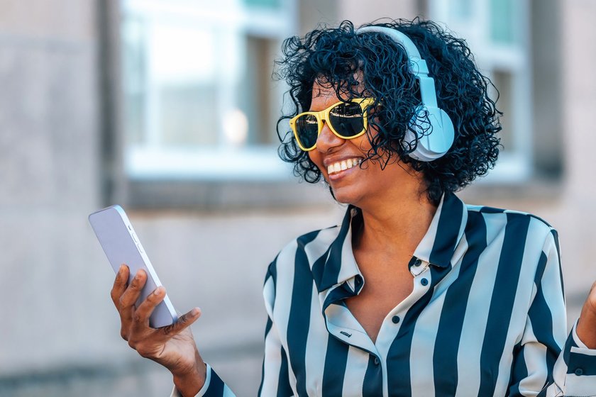Gen X Stärken: Lachende Frau mit Headphones und Handy Gen X Stärken: Lachende Frau mit Headphones und Handy