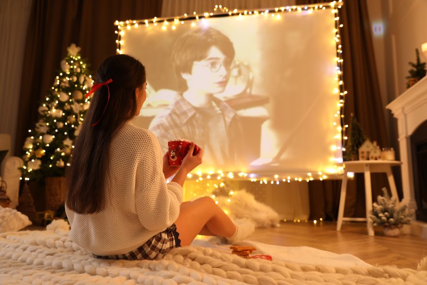 MYKOLAIV, UKRAINE - DECEMBER 24, 2020: Woman watching Harry Potter and Philosopher's Stone movie via video projector in room. Cozy winter holidays atmosphere