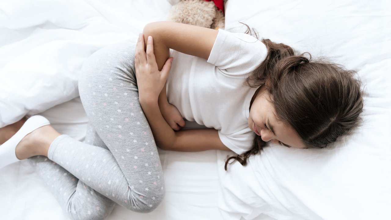 Bauchschmerzen bei Kindern: Mädchen liegt auf dem Bett und hat Schmerzen