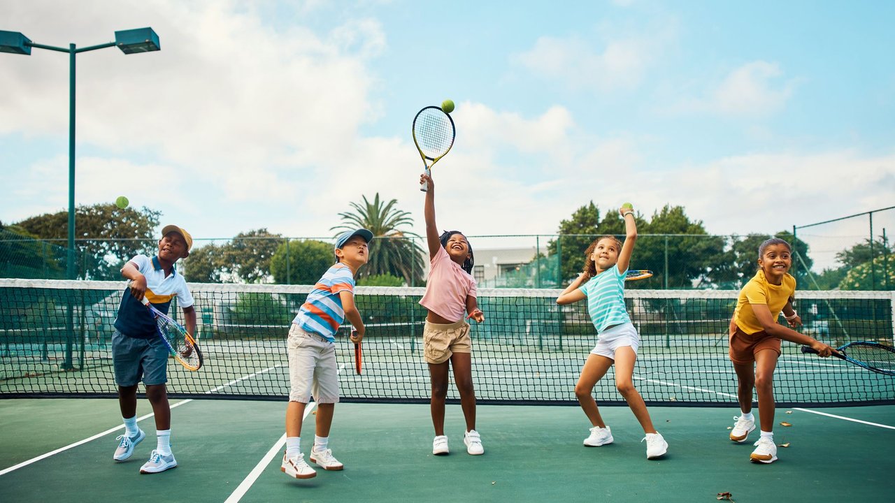 Tennis für Kinder: Fünf Kinder trainieren zusammen Tennis spielen auf dem Tennisplatz