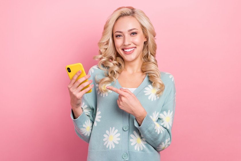 Photo of young joyful blogger lady wear flower print shirt indicate finger new design apple iphone promo isolated on pink color background. Photo of young joyful blogger lady wear flower print shirt indicate finger new design apple iphone promo isolated on pink color background.