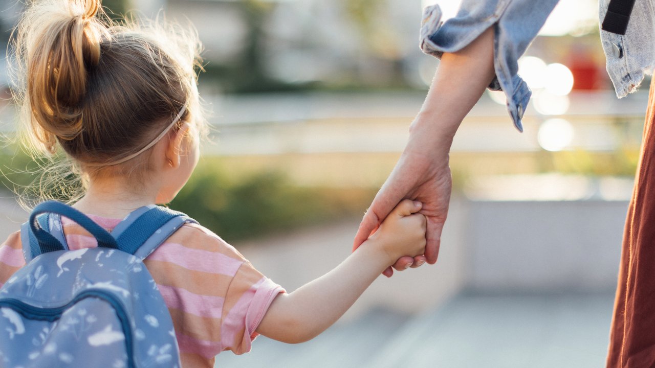 Back view of little girl with backpack holding a mom hand while walking to the school together. Back view of little girl with backpack holding a mom hand while walking to the school together.
