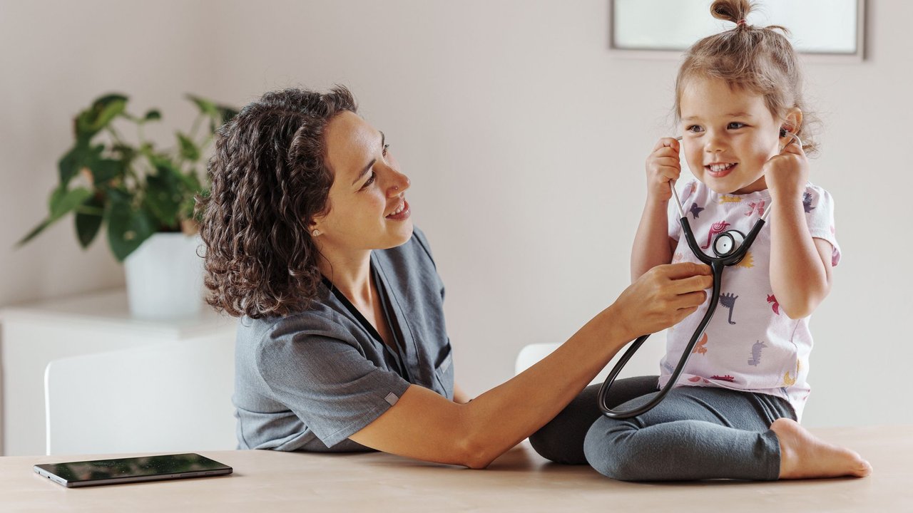Puls bei Kleinkindern: Frau misst bei kleinem Mädchen den Puls mit einem Stetoskop