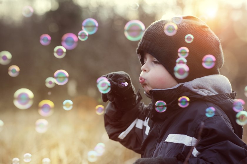 Little boy playing with bubble wand blowing soap bubbles