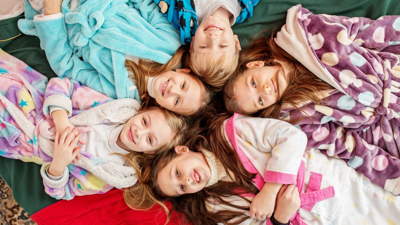 Fünf Kinder liegen bei ihrer Übernachtungsparty fröhlich zusammen im Bett.