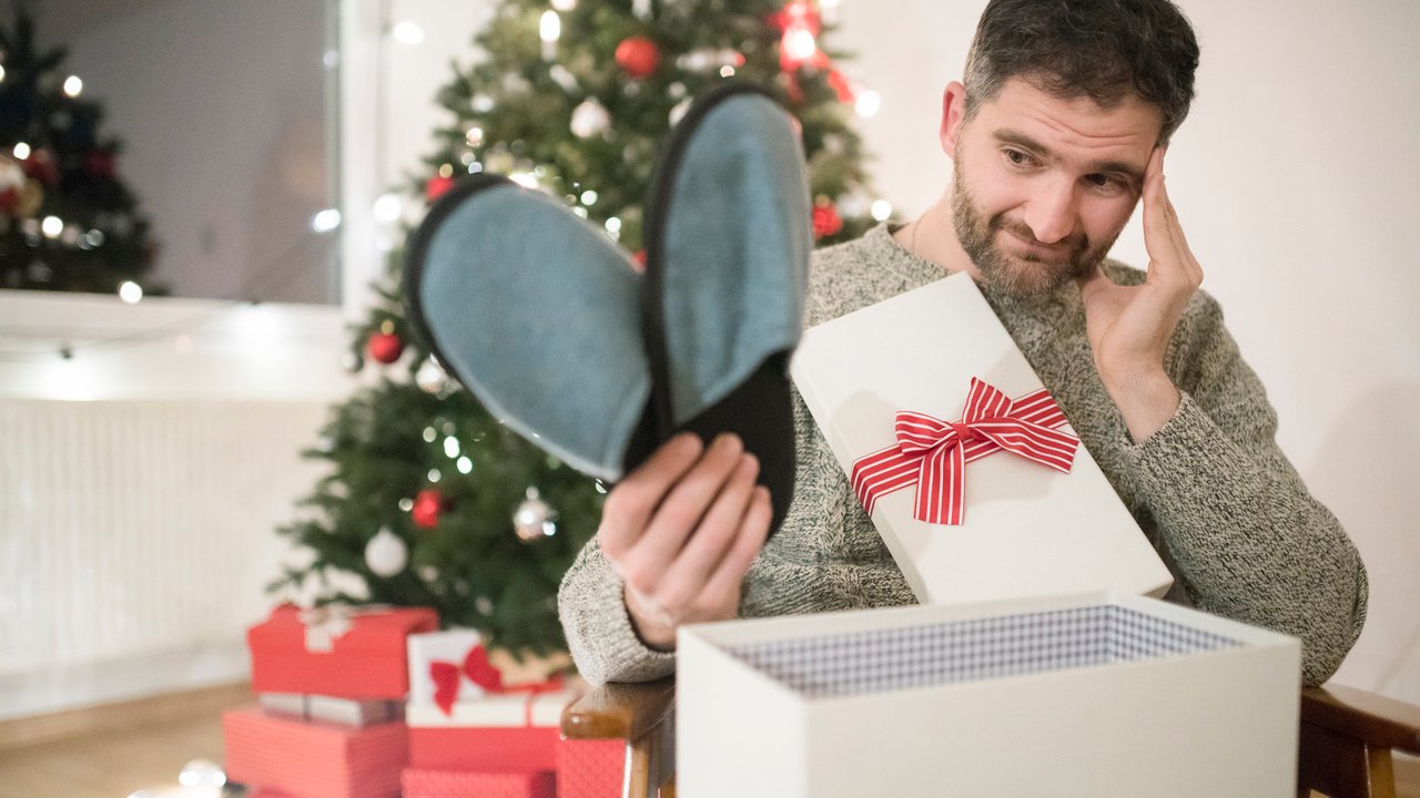 Mann öffnet enttäuscht ein Weihnachtsgeschenk