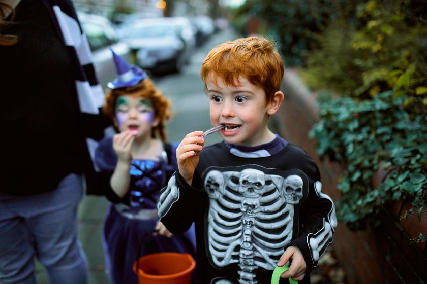 Kleiner Junge, der Halloween-Süßigkeiten isst, während er mit seiner Mutter und seiner Schwester in den Vorstadtstraßen Süßigkeiten sammelt. Kleiner Junge, der Halloween-Süßigkeiten isst, während er mit seiner Mutter und seiner Schwester in den Vorstadtstraßen Süßigkeiten sammelt.