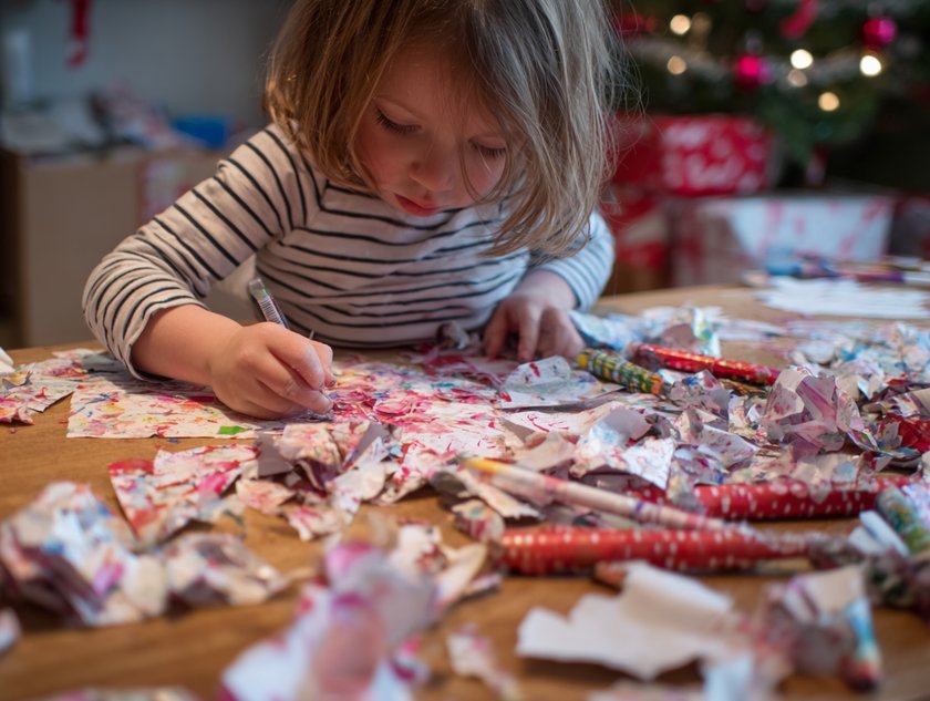 Spiele für Kinder für die Feiertage: Mädchen bastelt mit Geschenkpapier