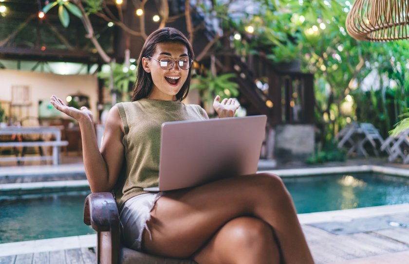 Junge aufgeregte Frau mit Notebook erhält tolle Nachricht am Pool