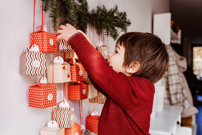 Glücklicher kleiner Junge öffnet Adventskalender