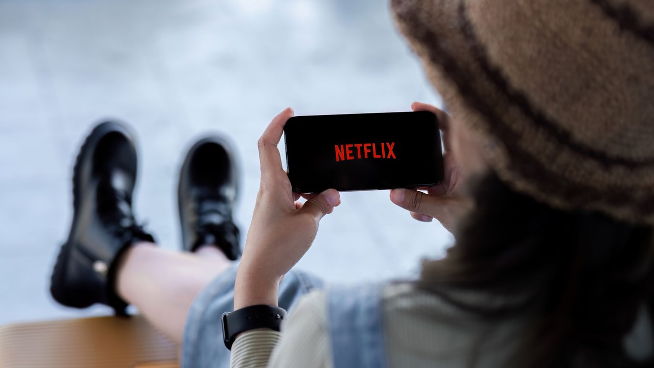 Welche Netflix-Serie soll ich als nächstes schauen? Frau sitzt entspannt mit Füßen hoch und freut sich auf ihre nächste Netflix-Serie auf dem Handy.