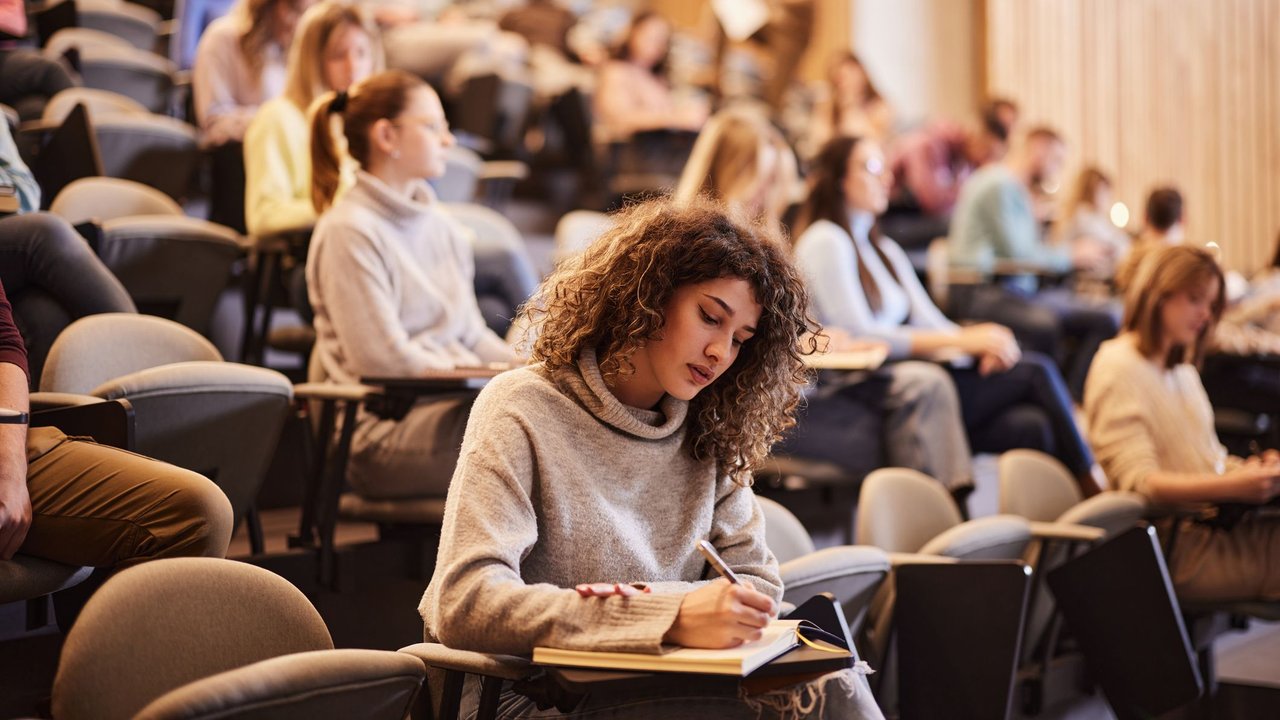 Frau sitzt in einem Hörsaal an der Universität und macht sich Notizen