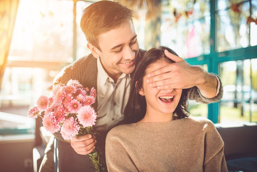 Blumen und ihre Bedeutung: Mann mit Blumenstrauß hält Frau die Augen zu