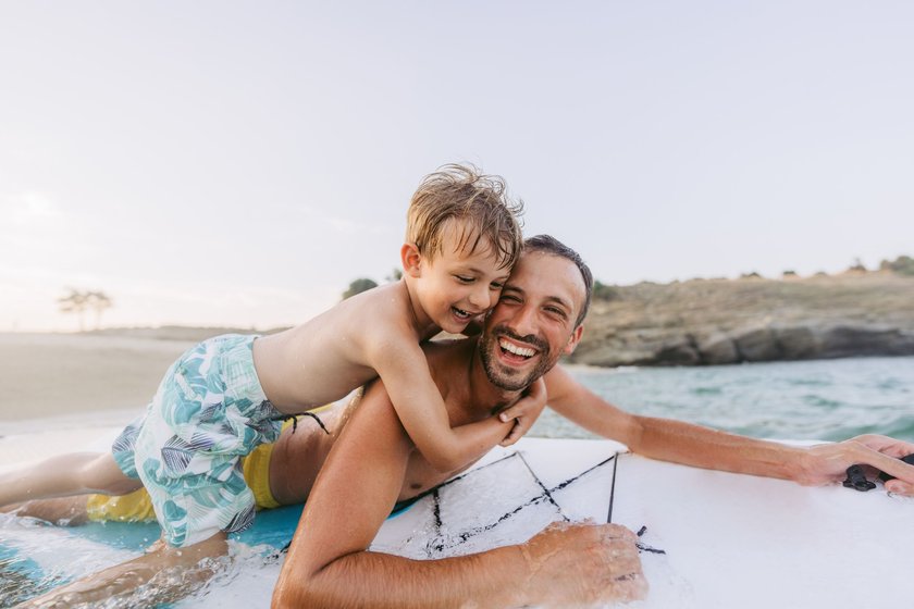 Vater und Kind auf einem Surfboard am Strand