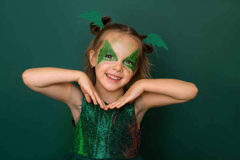 Funny comical girl with a pattern around her eyes in the image of a dragon on a green background. Aquagrim on a child's face