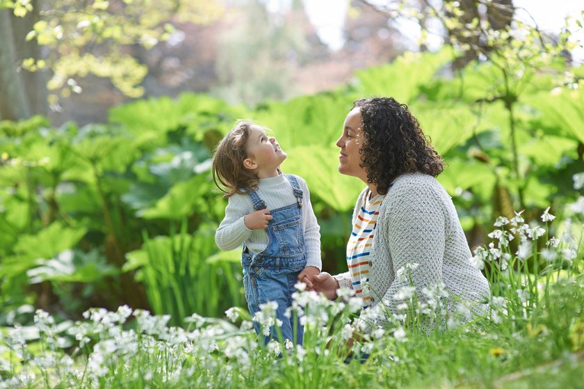 A happy mother and daughter sit amongst the snowdrops growing in an idyllic park as they learn about nature and the environment.