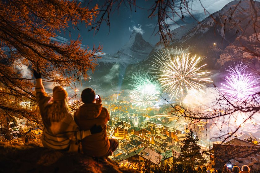 Pärchen sitzt auf einem Berg und beobachtet von oben das Feuerwerk