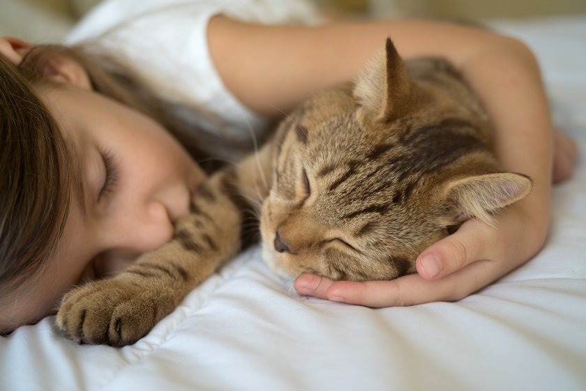 Mädchen schläft mit Katze im Arm