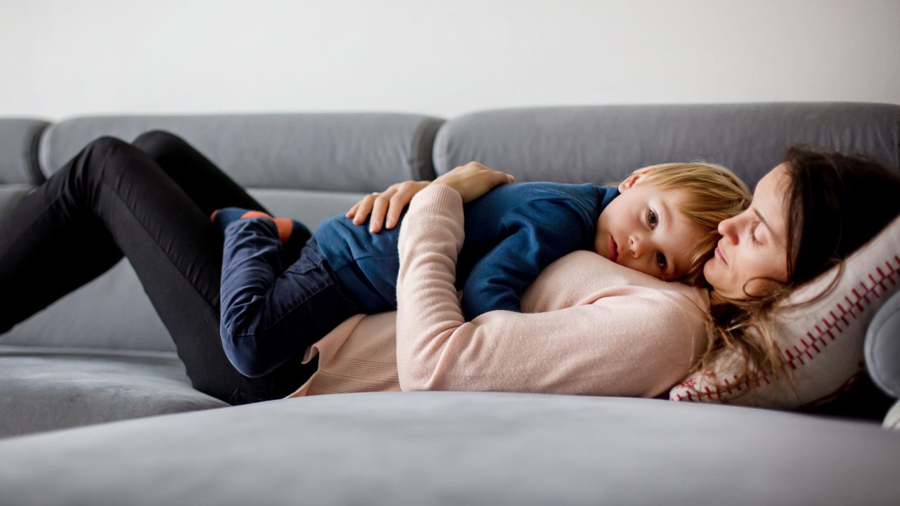 Fieber geht nicht runter: Mama kuschelt mit krankem Kind auf dem Sofa