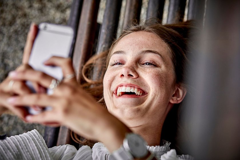 Lachendes Mädchen mit ihrem Handy auf einer Bank im Freien