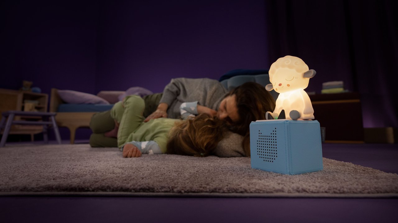 Schlaflieder Tonie: Mutter mit Kind kuschelt neben blauer Toniebox mit leuchtendem Schaf
