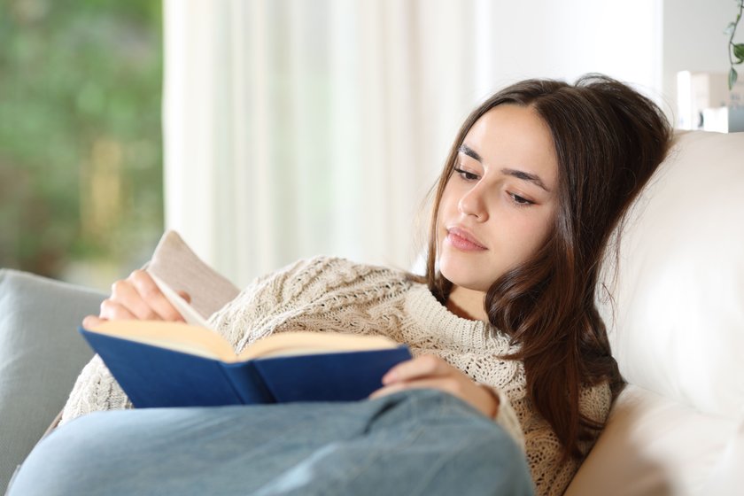 Serious woman reading paper book on a couch