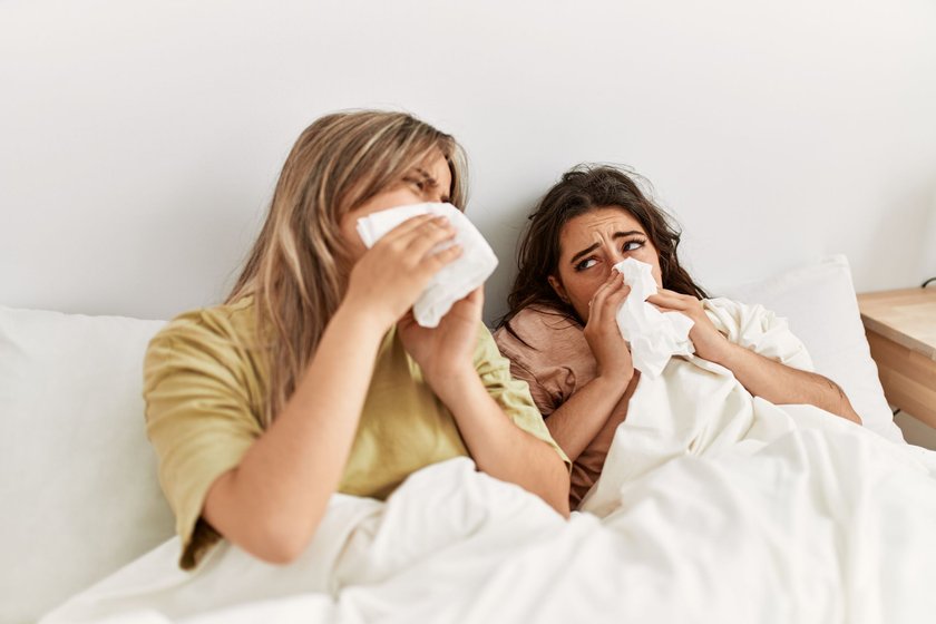 Junges krankes Paar, das zu Hause auf dem Bett liegt und eine Serviette benutzt.