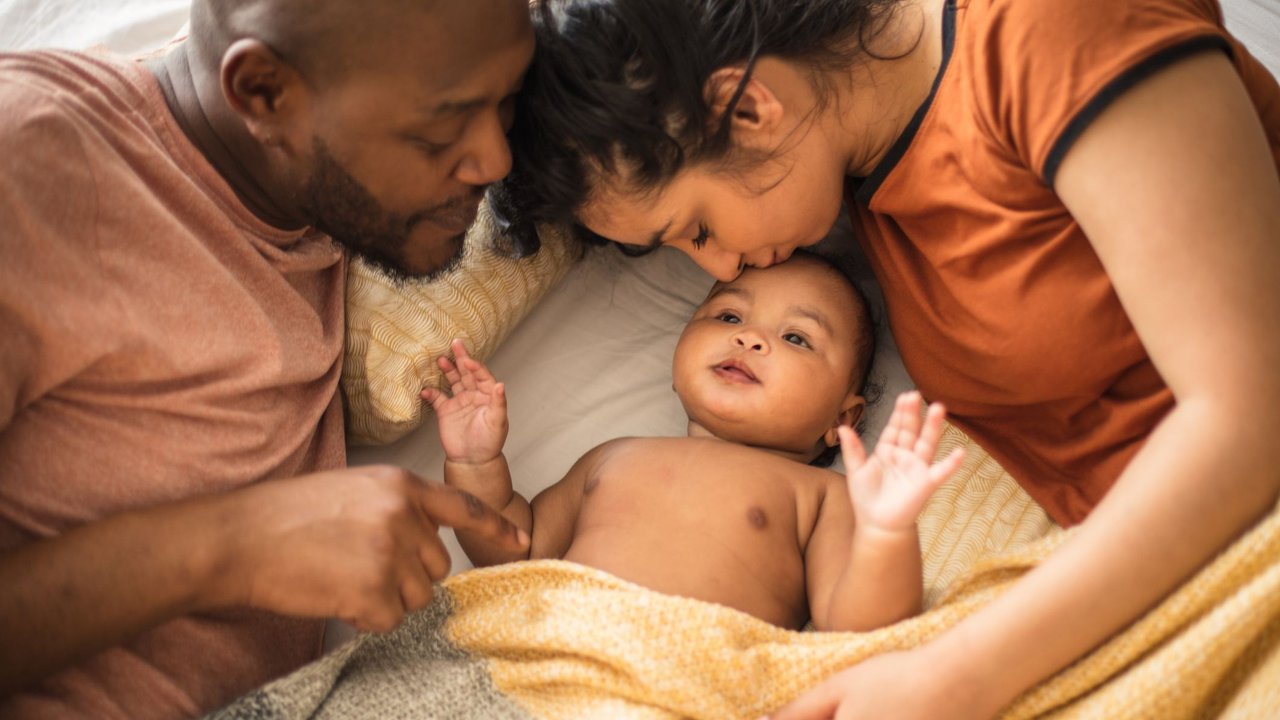 Elternzeit beantragen: Mama und Papa kuscheln mit Baby