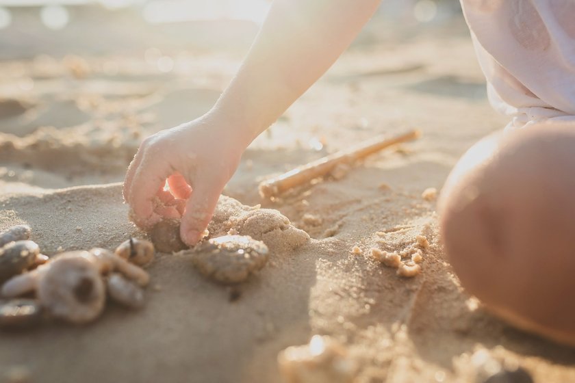 Mit dem Baby sicher durch den Sommer: Kind spielt am Strand mit Muscheln