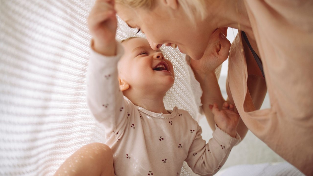 Mutter und Baby-Tochter spielen vergnügt unter einer weißen Decke