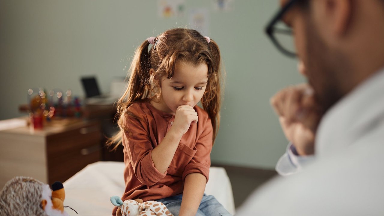 Cute little girl coughing during a medical exam with her pediatrician in hospital.