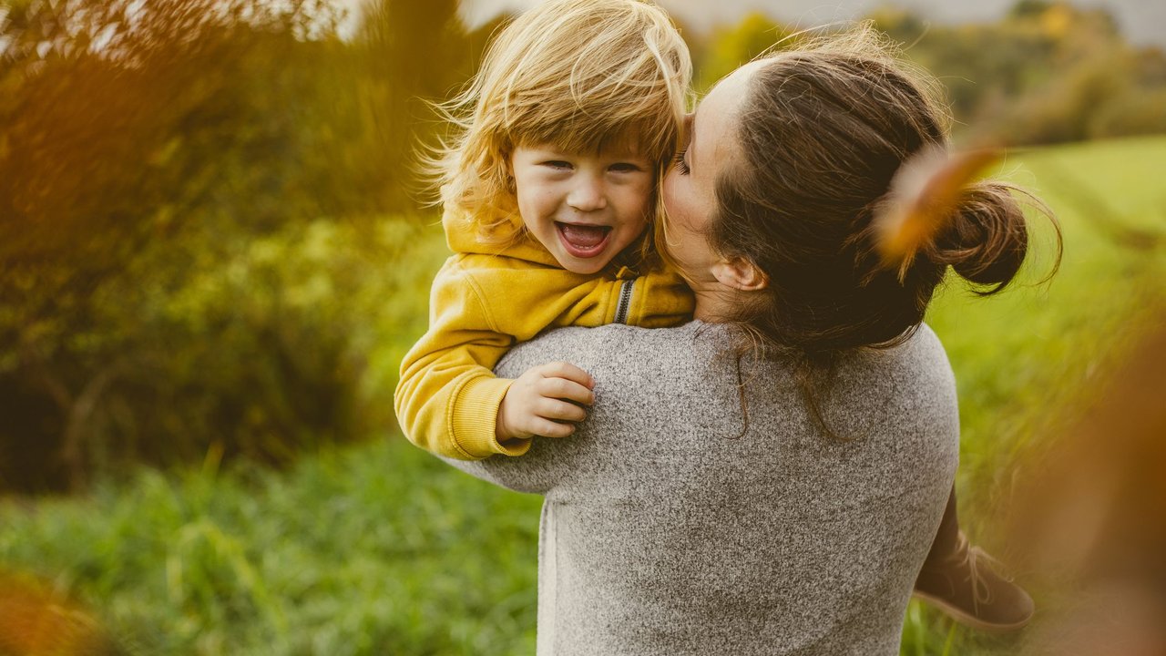 Mutter setzt Kind auf Zuckerdiät und tobt mit ihm fröhlich in der Natur. Das Kind lacht glücklich. (Symbolfoto)