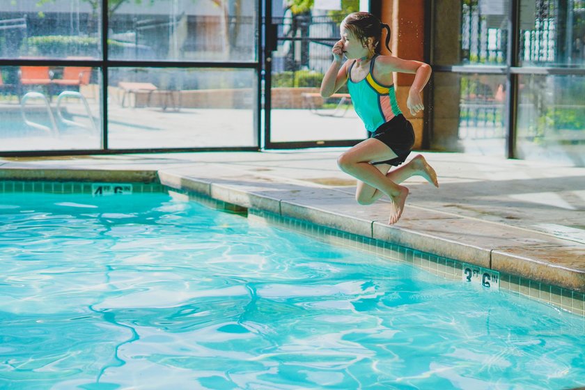 a little girl learning to swim, and jumping courageously into the blue water alone at the pool