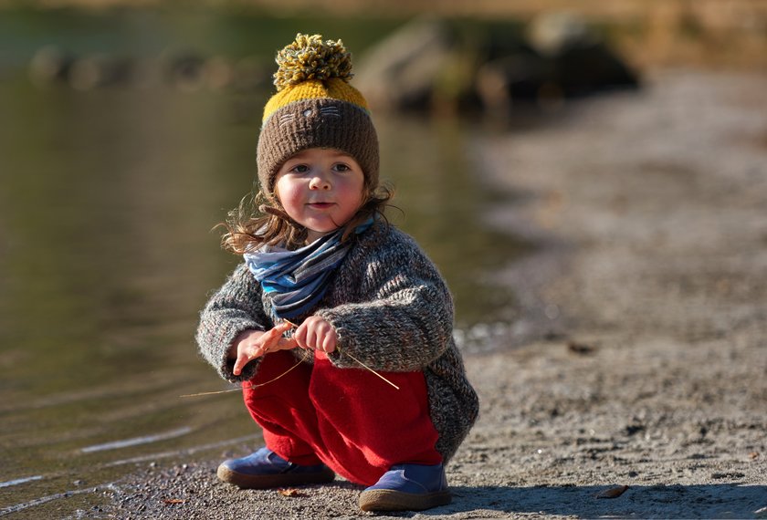 Little baby girl at the lake, playing on the edge of water, touching, looking away