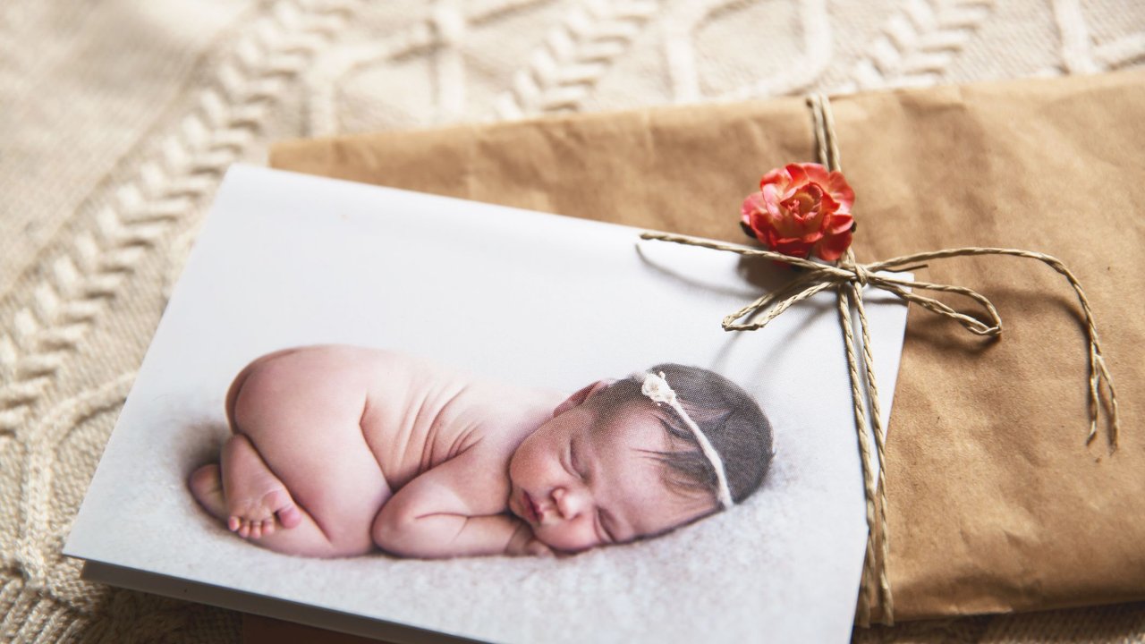 Geldgeschenke zur Geburt: In Packpapier eingeschlagenes Geschenk darauf eine Karte mit kleinem Baby und Blume