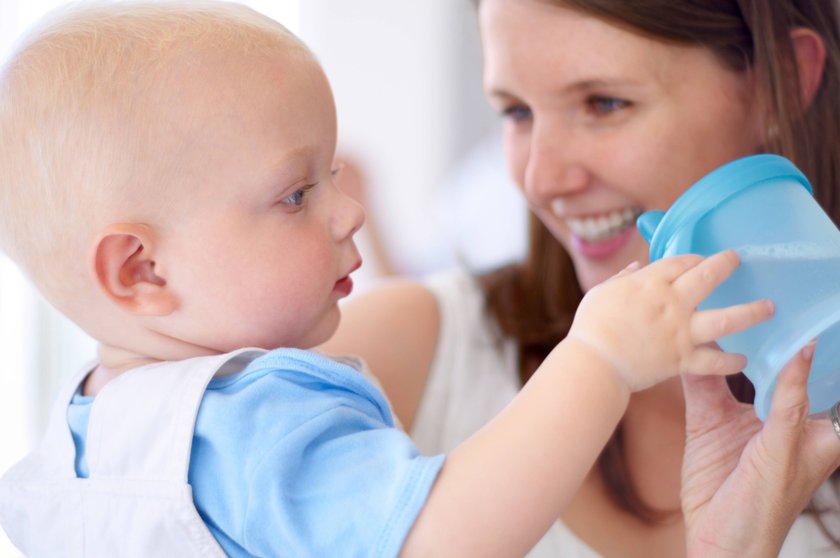 Playing, happy and a mother with a baby and water, bonding and care with a drink in a house