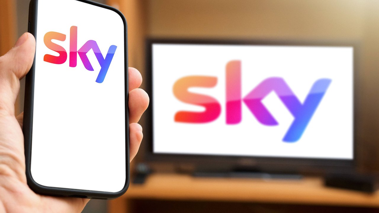 6 April 2024: Hand holding smartphone in front of TV screen with the Sky pay TV and streaming provider logo. PHOTOMONTAGE *** Hand hält Smartphone vor TV Bildschirm mit dem Pay-Tv und Streaming Anbieter Logo von Sky. FOTOMONTAGE