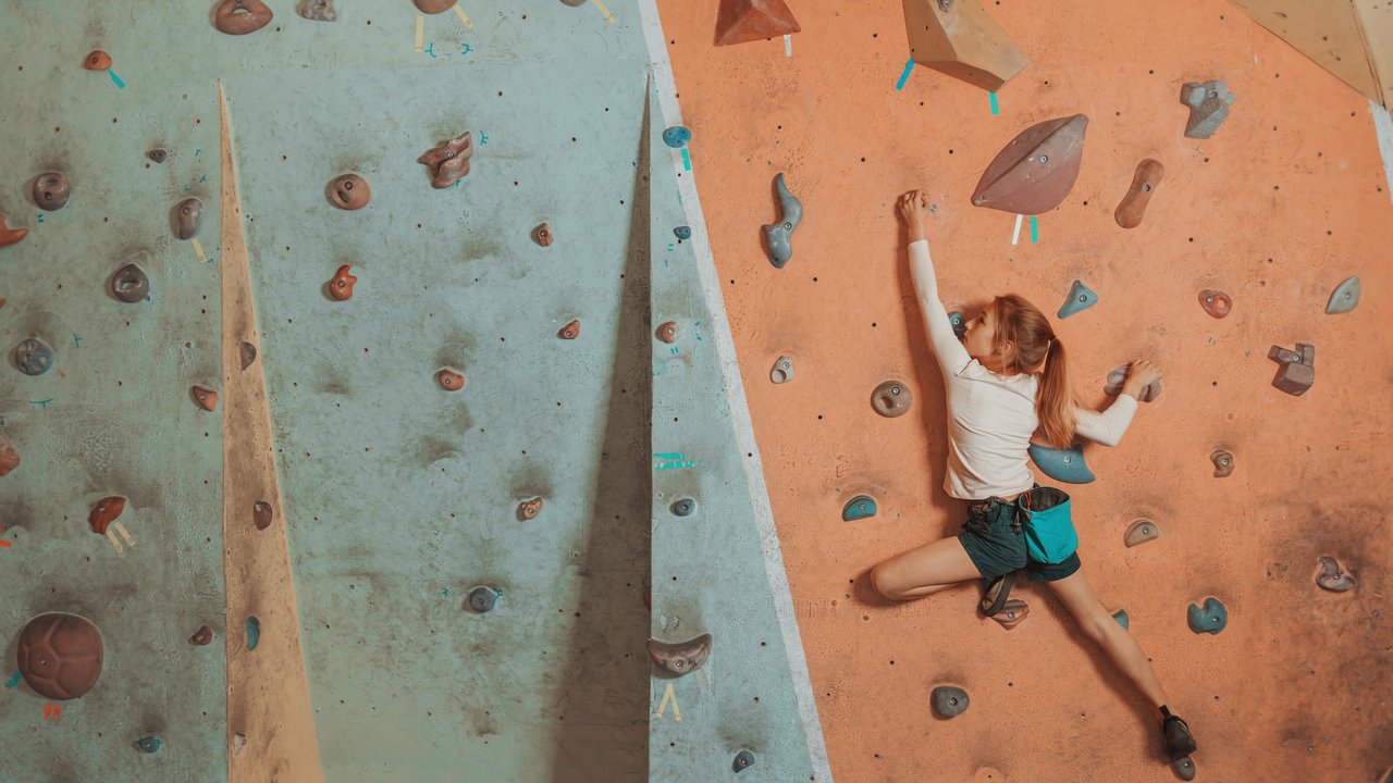 Sporty little girl climbing artificial boulder on practical wall in gym