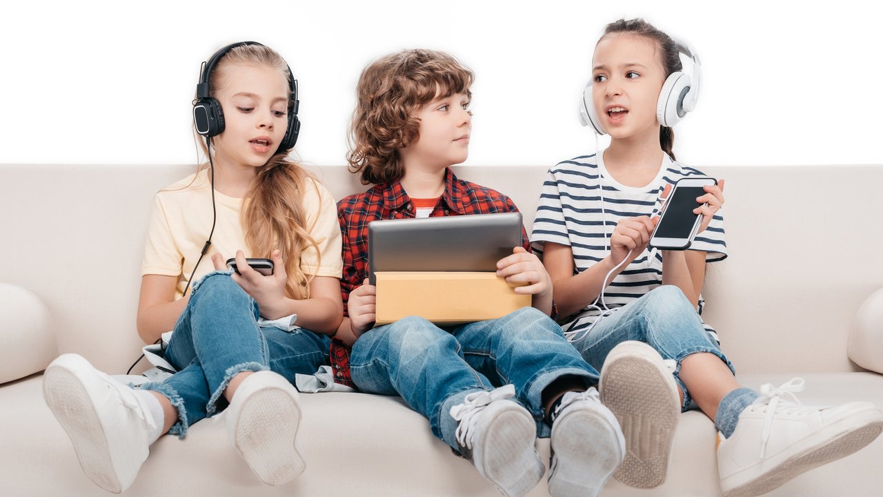 Cute kids using digital devices, listening music while sitting on couch