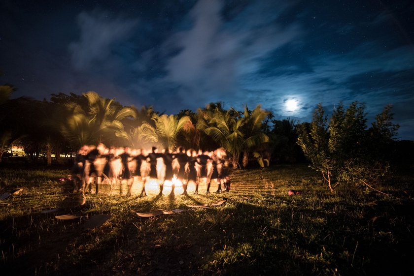 Menschen tanzen um ein Lagerfeuer in den Tropen bei Vollmond