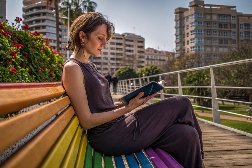 Poesiealbum-Sprüche: Frau sitzt auf Regenbogenbank im Freien und liest in Buch