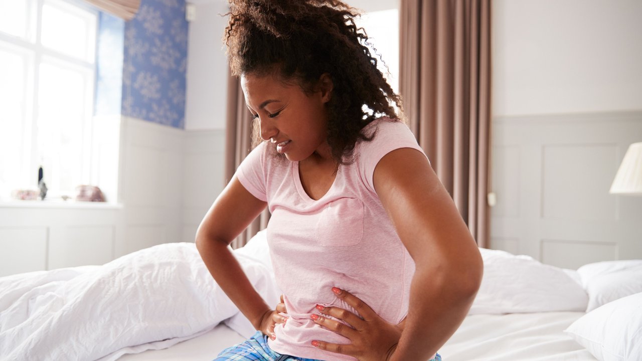 Woman Wearing Pajamas Suffering With Period Pain Sitting On Bed At Home